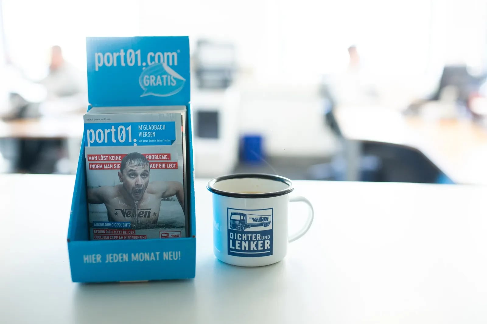 Tresenaufsteller des Stadtmagazins port01 neben einer bedruckten Emailletasse.
